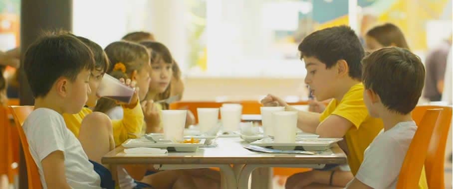 Crianças fazendo refeição à mesa no restaurante da escola
